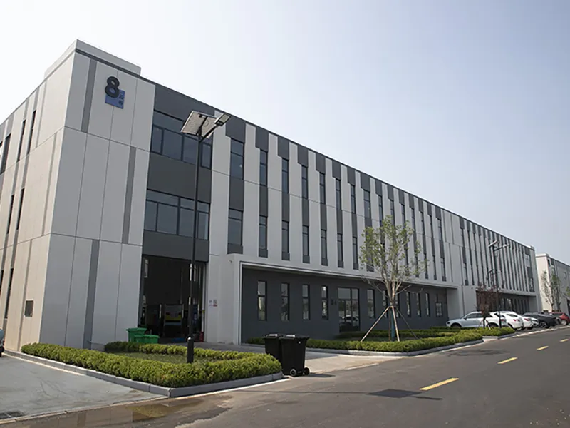 A modern multi-story industrial building with a sleek grey and white facade, solar street lights, and landscaped grounds.
