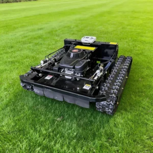 Front side view of a black remote-controlled tracked lawn mower with a gasoline engine, resting on a lush green grass field.