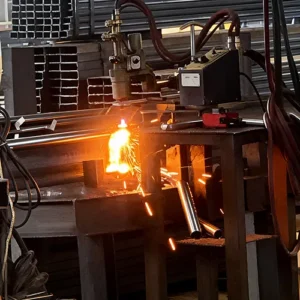 Close-up view of a flame cutting torch cutting a metal pipe, producing sparks and molten metal in a factory workshop.