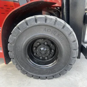 Close-up view of a solid rubber forklift tire mounted on a red forklift, with an outdoor concrete ground background.