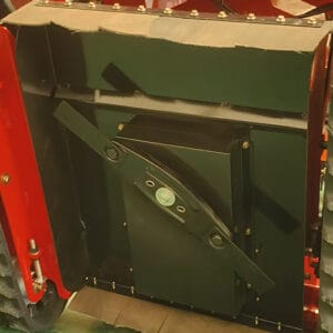 Close-up view of a lawn mower cutting deck assembly with adjustable blade mechanism, installed in a red tracked lawn mower, in a factory workshop.