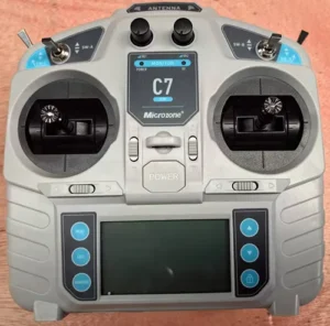Front view of a Microzone C7 remote controller with dual joysticks and a display screen, placed on a wooden table.