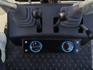 Close-up of a black mini excavator control panel with dual hydraulic joysticks, a digital hour meter, and a voltage gauge.
