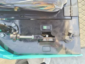 A top-down view of a black mini excavator control panel, showing an on-off rocker switch, an ignition key cylinder with keys, and a mechanical control linkage.