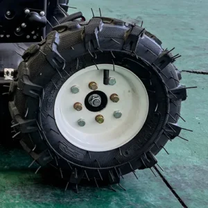 Close-up view of a rugged off-road tire with metal anti-slip spikes, mounted on a white wheel rim, on a green factory floor.