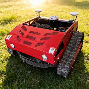 Front side view of a red remote-controlled tracked lawn mower with dual GPS antennas and LED headlights, operating on a sunlit grass field.