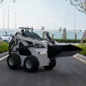 Front side view of a white mini wheeled skid steer loader with black bucket attachment and control joysticks, operating on a paved outdoor road.