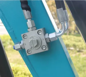 Close-up of hydraulic control valve block mounted on teal mini excavator boom with fittings