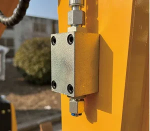 Close-up of hydraulic control valve on yellow mini excavator boom with fittings and bolts