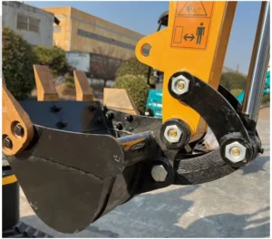 Close-up of mini excavator bucket, teeth and linkage joints with warning label