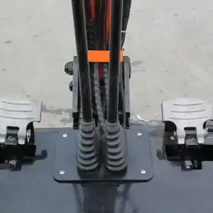 Close-up shot of a mini excavator's foot pedal control system, showing hydraulic levers, footrests and cable routing for construction equipment.