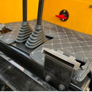 Close-up of mini excavator's foot pedal controls with quilted cabin mat and red safety lever for construction equipment