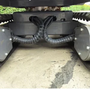 Close-up of mini excavator undercarriage showing protected hydraulic hoses and tracked chassis