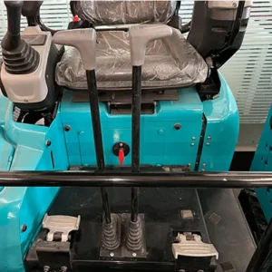 Close-up of turquoise mini excavator cabin showing control levers, foot pedals and operator seat with protective cover