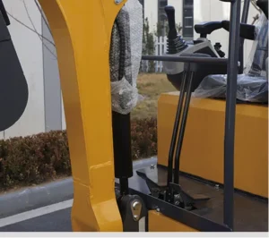 Close-up of yellow mini excavator boom cylinder, hydraulic hoses and operator foot pedals
